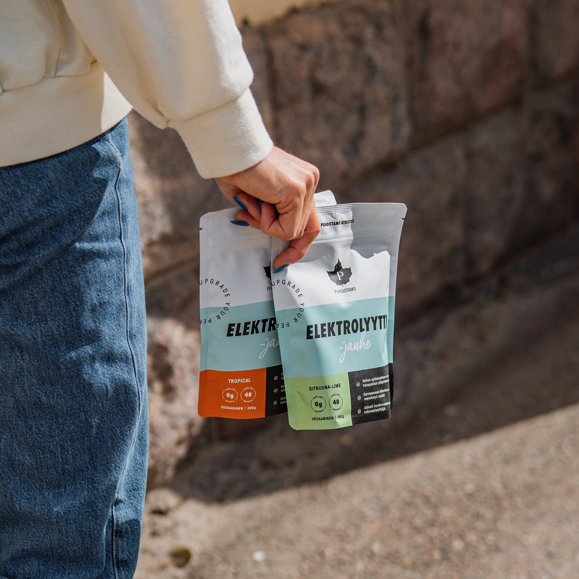 A person holding two packets of electrolytes outdoors.