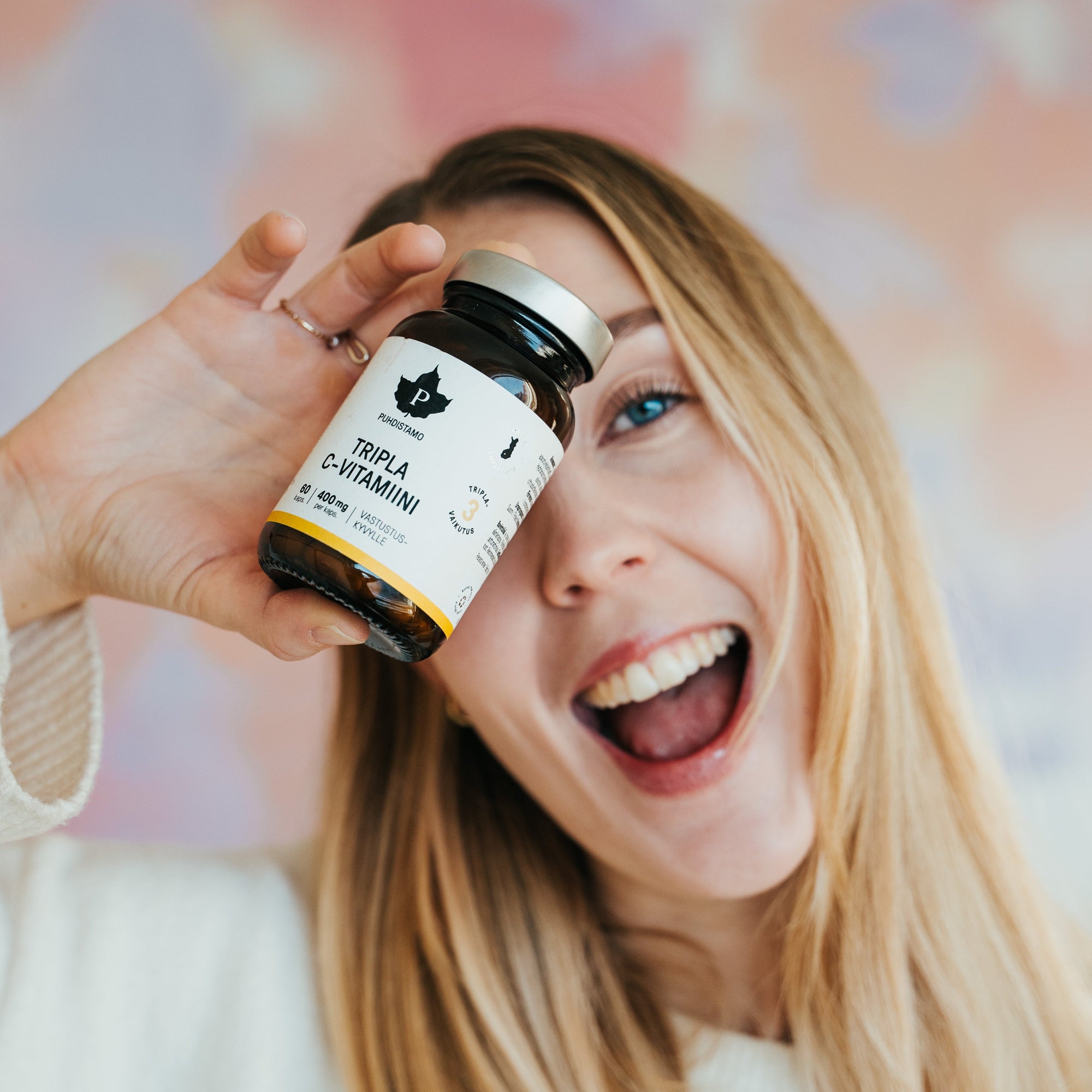 Smiling woman holding a bottle of vitamins in front of a colorful background.