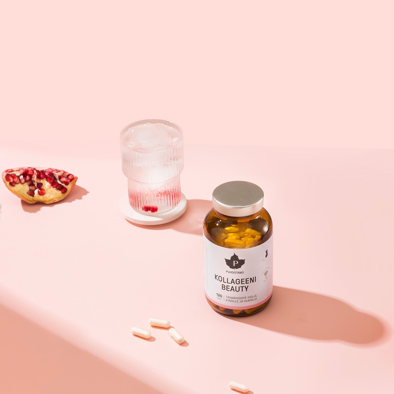 Collagen supplement bottle next to a glass of water and pomegranate.