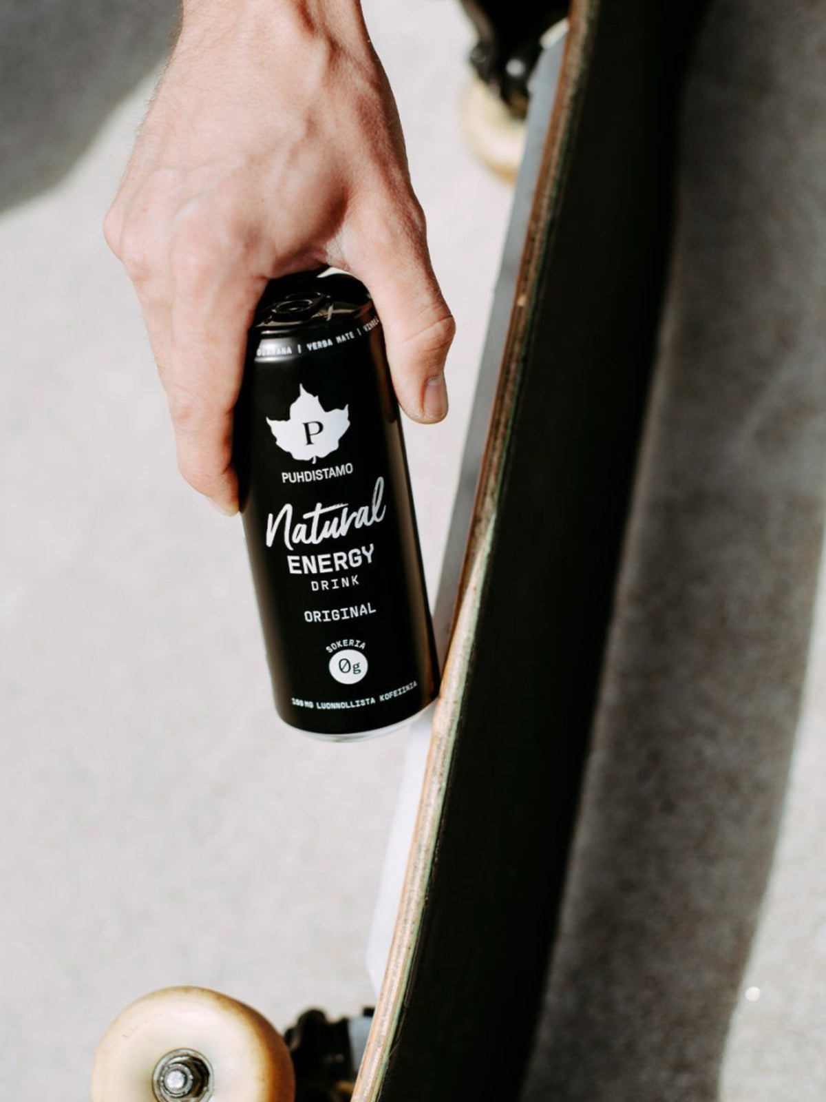 Mies pitää kädessään Puhdistamon Natural Energy Drink Original -purkkia ja skeittilautaa