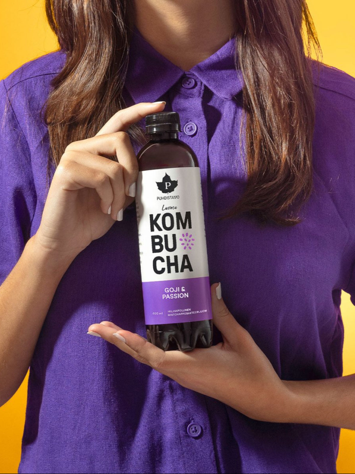 Nainen pitää kädessään Puhdistamon Luomu Kombucha Goji - Passion pulloa