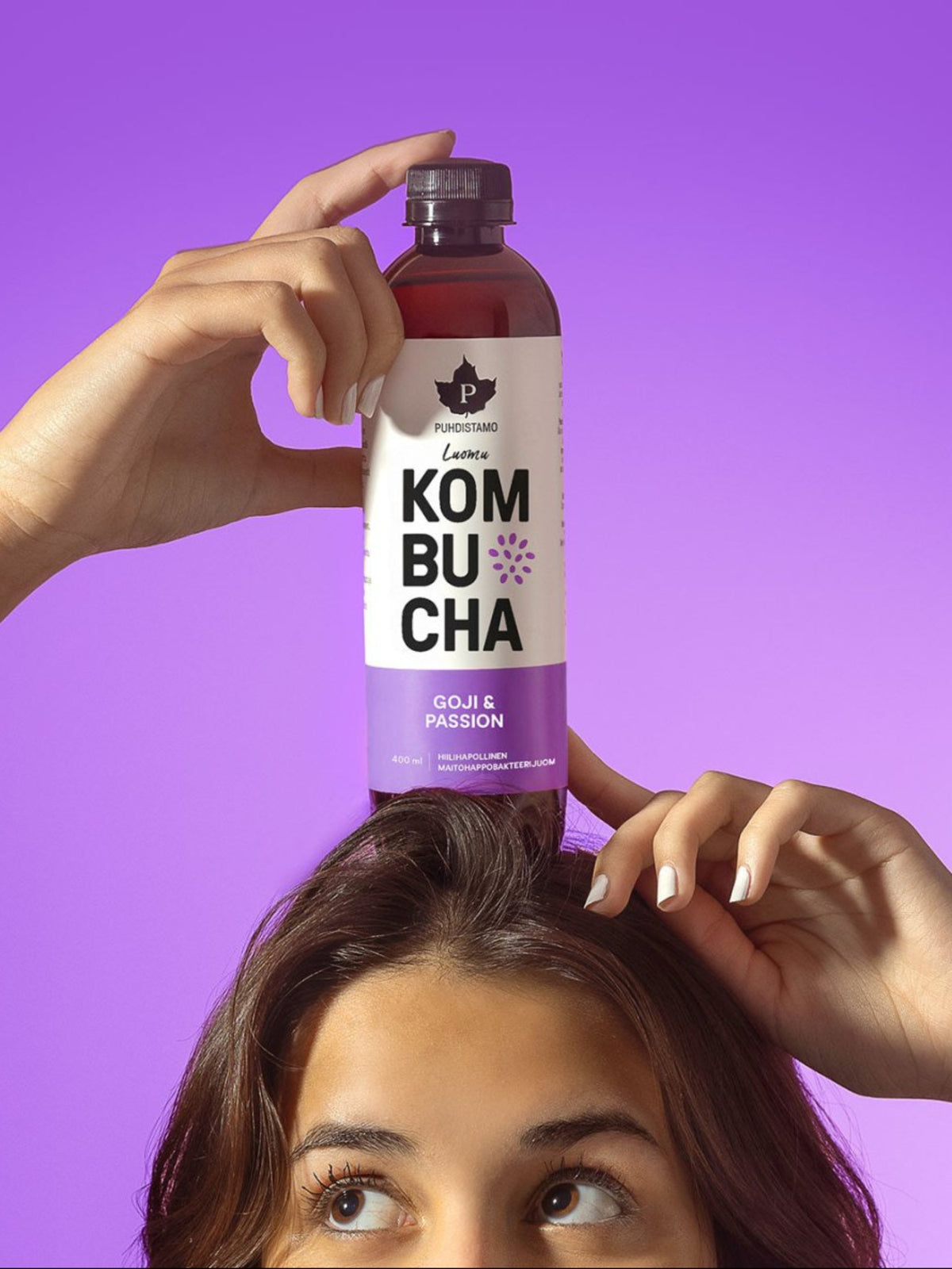 Nainen pitää päänsä päällä Puhdistamon Luomu Kombucha Goji-passion pulloa