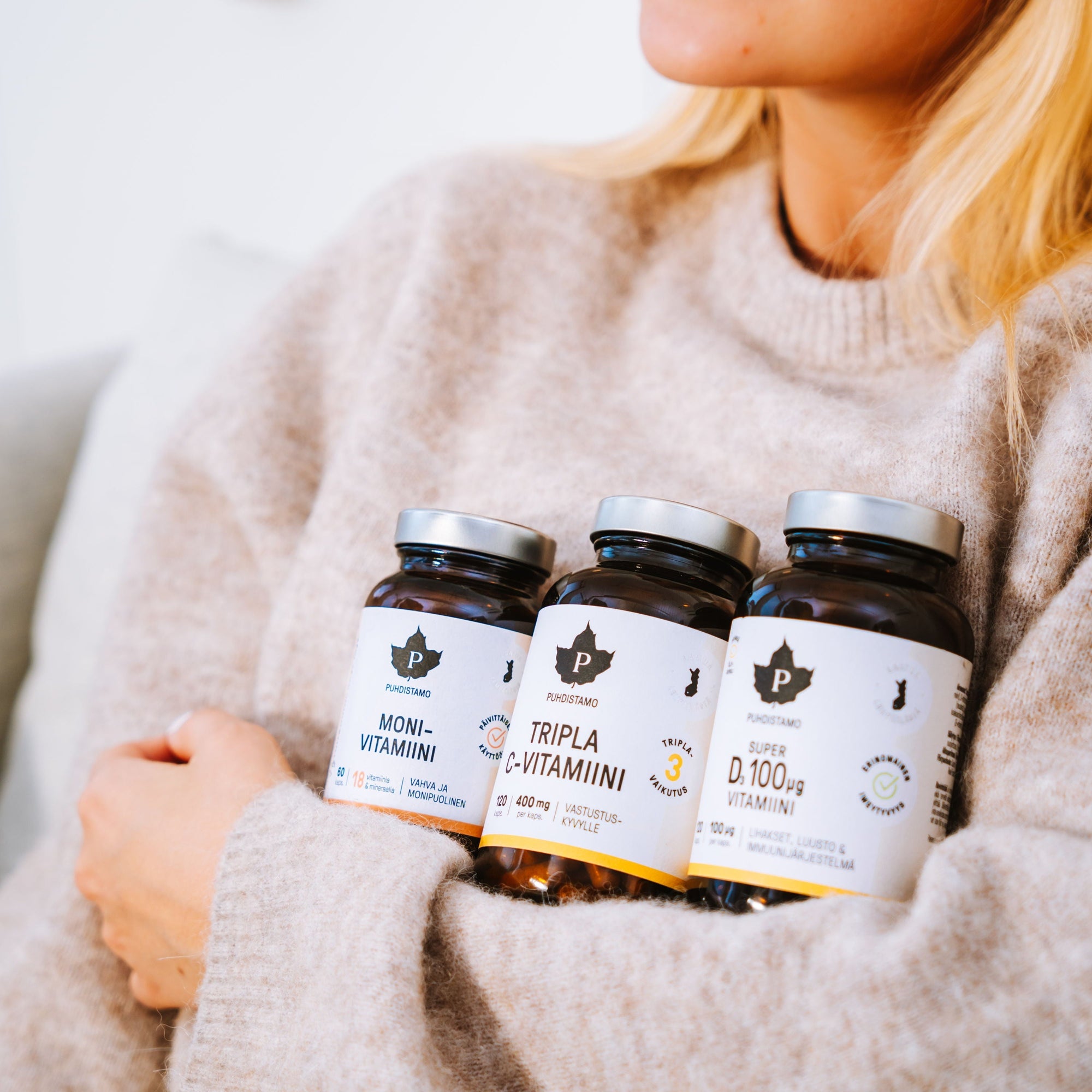 A woman in a sweater holding three bottles of supplements.
