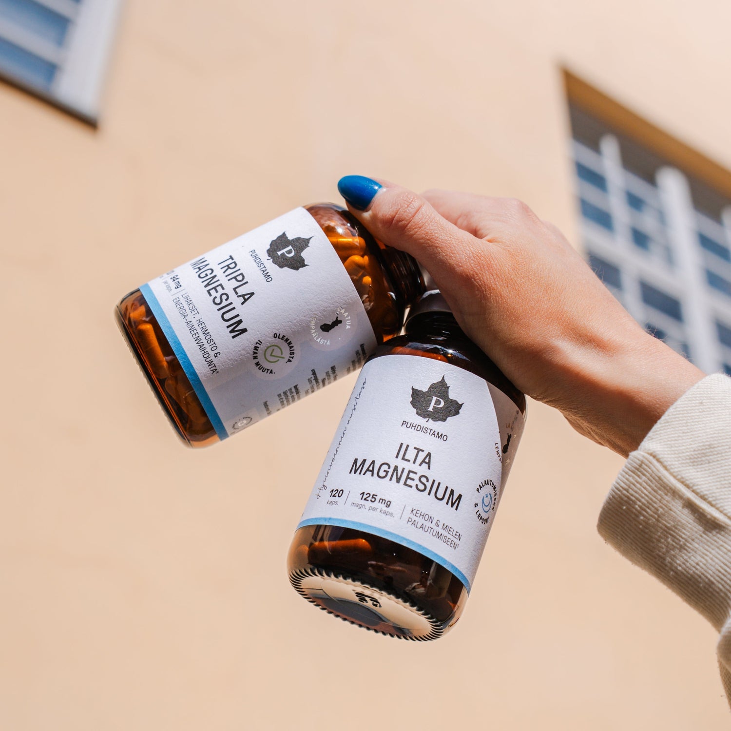 Person holding two bottles of magnesium supplements against a building background.