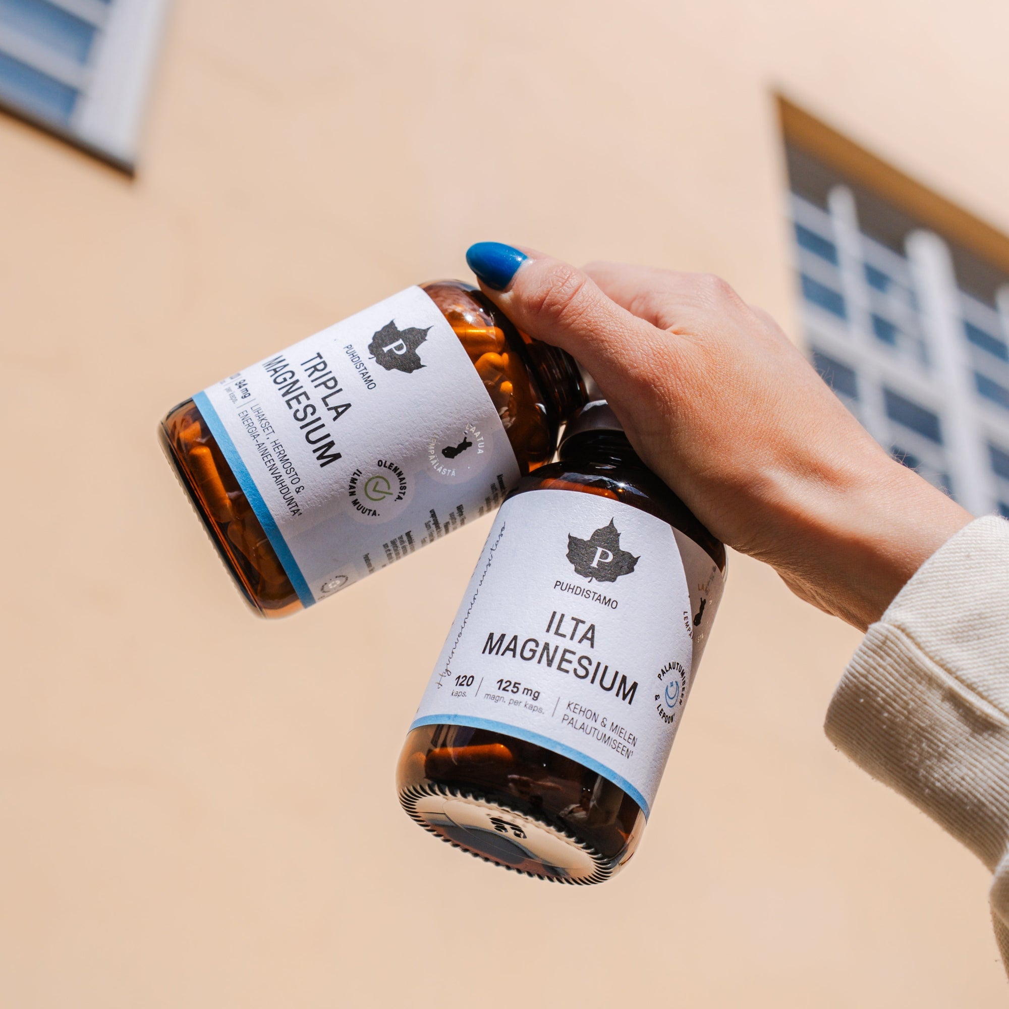 Person holding two bottles of magnesium supplements against a building background.