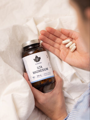 Nainen istuu sängyssä ja pitelee käsissään Puhdistamon Ilta Magnesium purkkia ja kapseleita