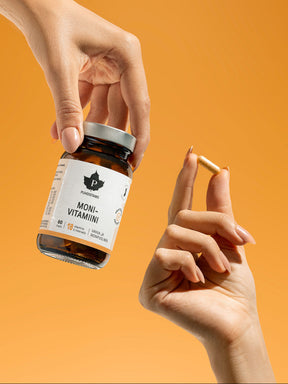 Käsi pitelee Puhdistamon monivitamiini purkkia ja kapselia