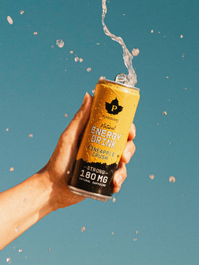 Nainen läiskyttää Puhdistamon Natural Energy Drink Pineapple Crush tölkkiä sinistä taivastga vasten