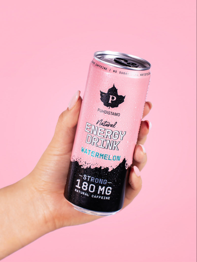 Naisen käsi pitelee Puhdistamon Natural Energy Drink Watermelon tölkkiä vaaleanpunaista taustaa vasten