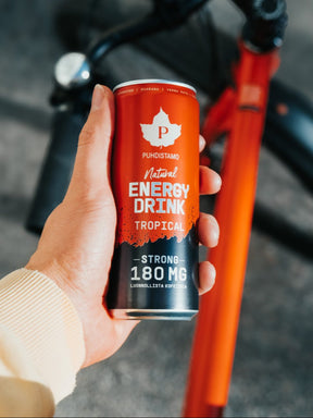 Mies pitelee kädessään Puhdistamon Natural Energy Drink Tropical Strong tölkkiä pyörä taustalla