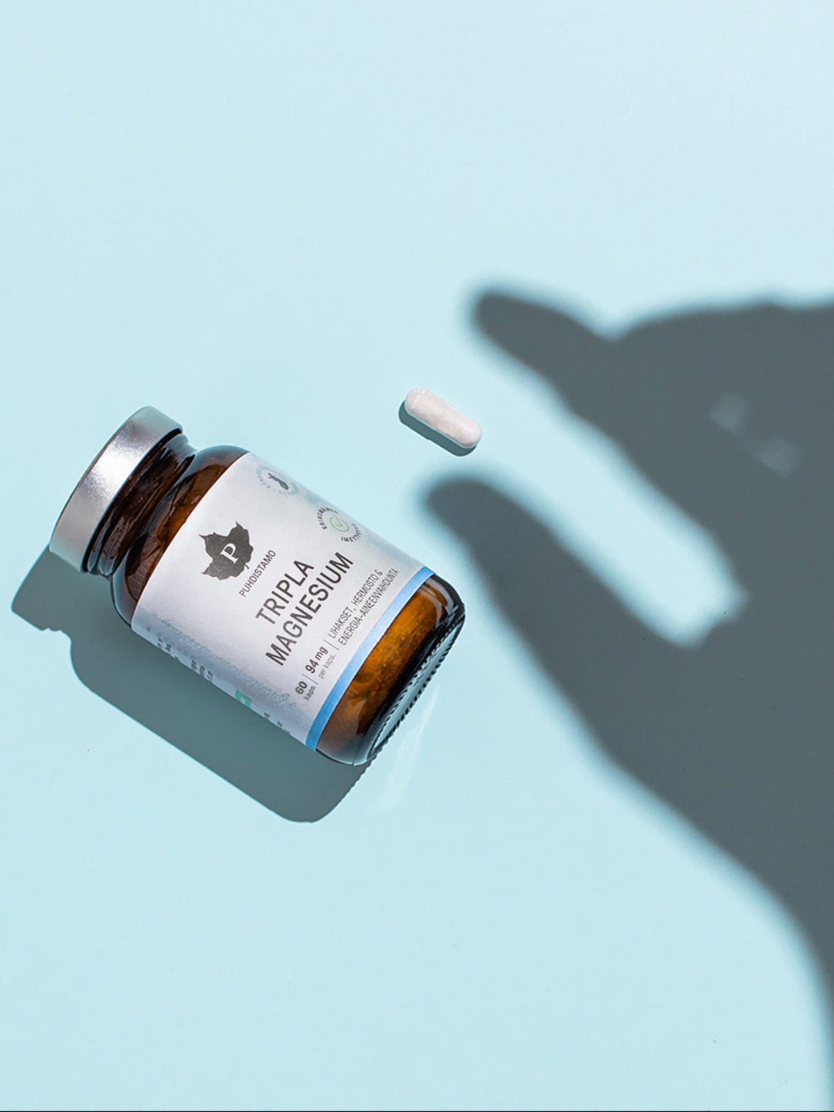 Puhdistamon Tripla Magnesium purkki vaaleansinisellä taustalla ja käden varjo