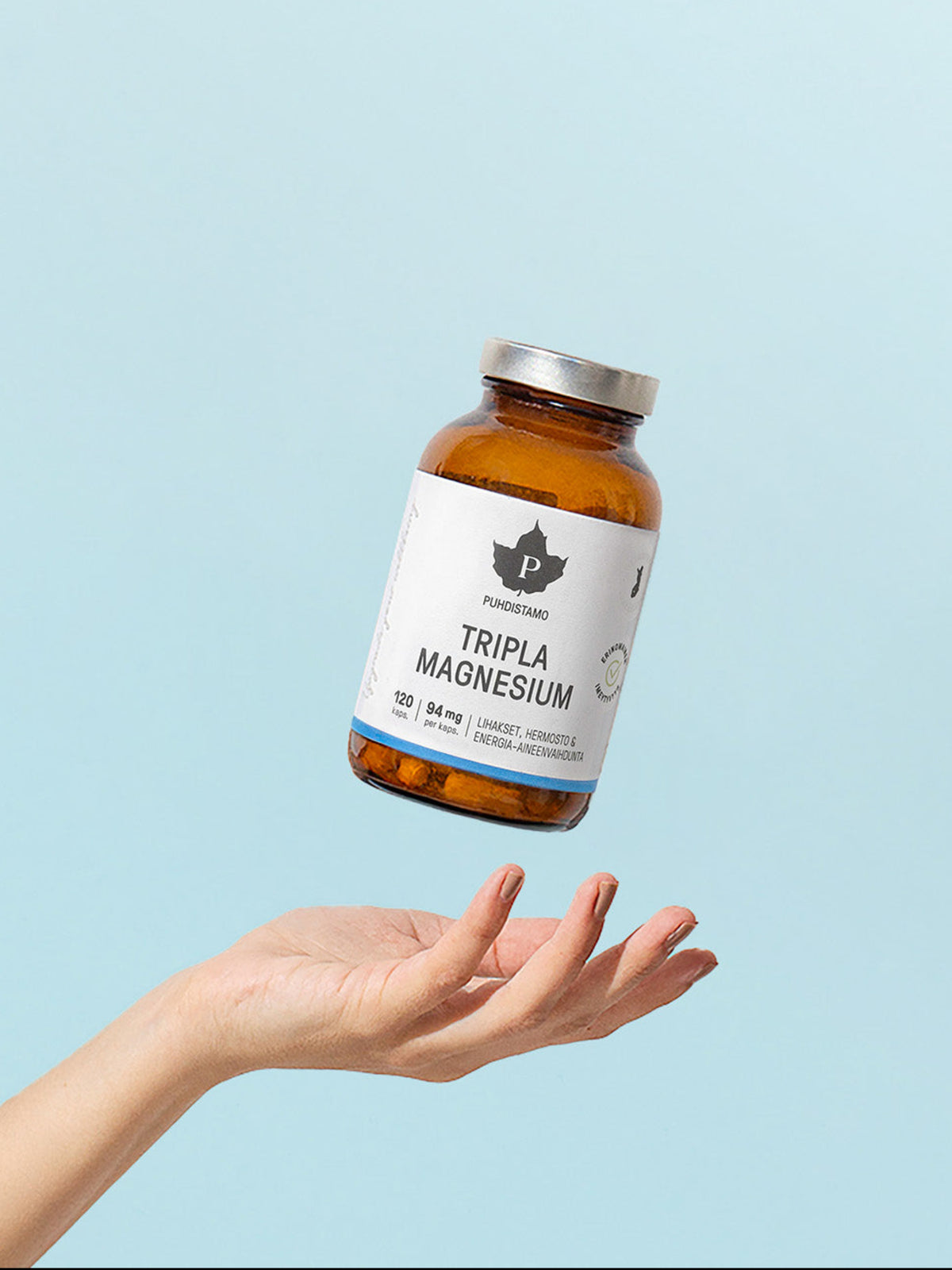 Naisen käsi ja Puhdistamon Tripla Magnesium purkki vaaleansinistä taustaa vasten