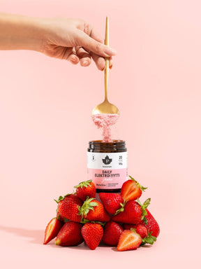 Nainen ottaa lusikalla jauhoja Daily Elektrolyyttijauhe Mansikka -purkista