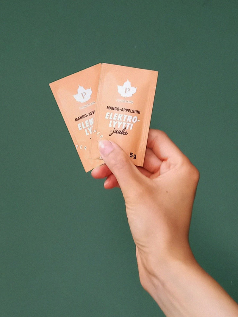 Nainen pitelee käsissään Puhdistamon Elektrolyyttijauhe Mango-appelsiini - Annospussia