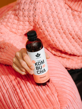 Nainen pitää kädessään Puhdistamon Luomu Kombucha persikka pulloa
