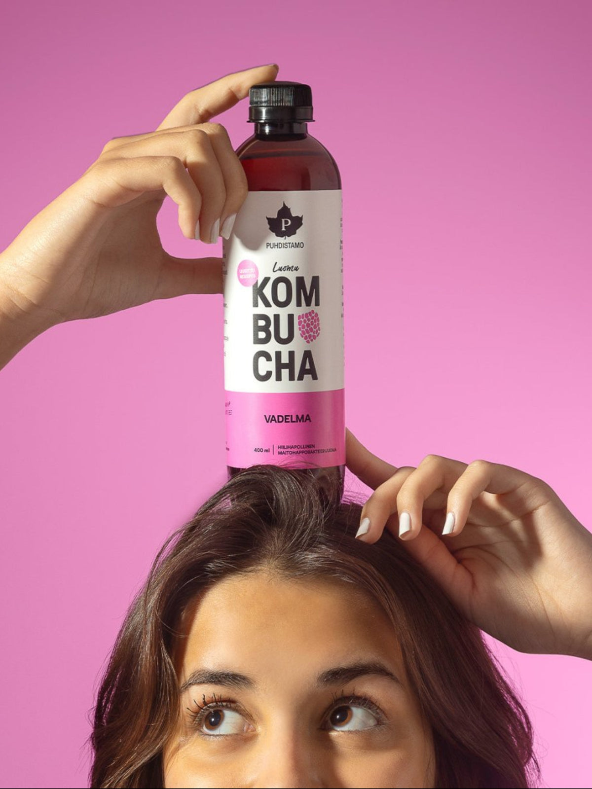 Nainen pitää päänsä päällä Puhdistamon Luomu Kombucha vadelma pulloa