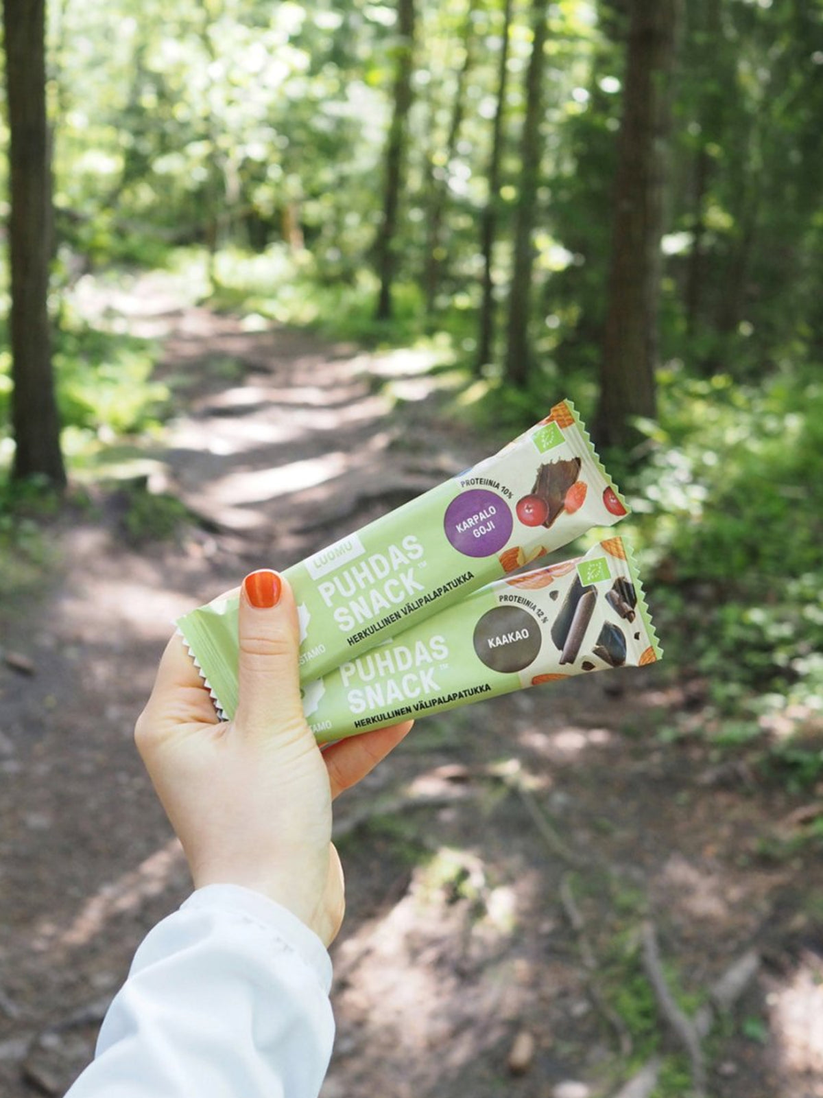 Nainen pitää kädessään kahta Puhdistamon Puhdas Snack™ patukkaa metsätiellä