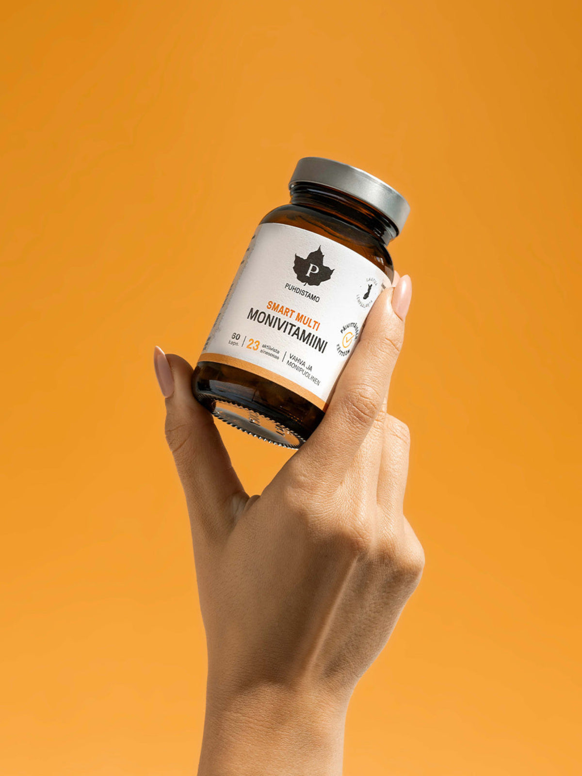 Nainen pitää kädessään Puhdistamon Smart Multi Monivitamiini oranssia taustaa vasten