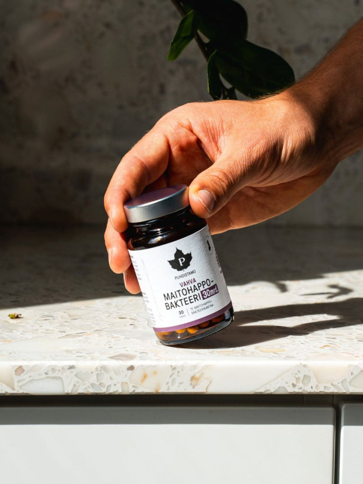 Mies nostaa pöydältä Puhdistamon Vahvan Maitohappobakteeri 30 mrd purkin