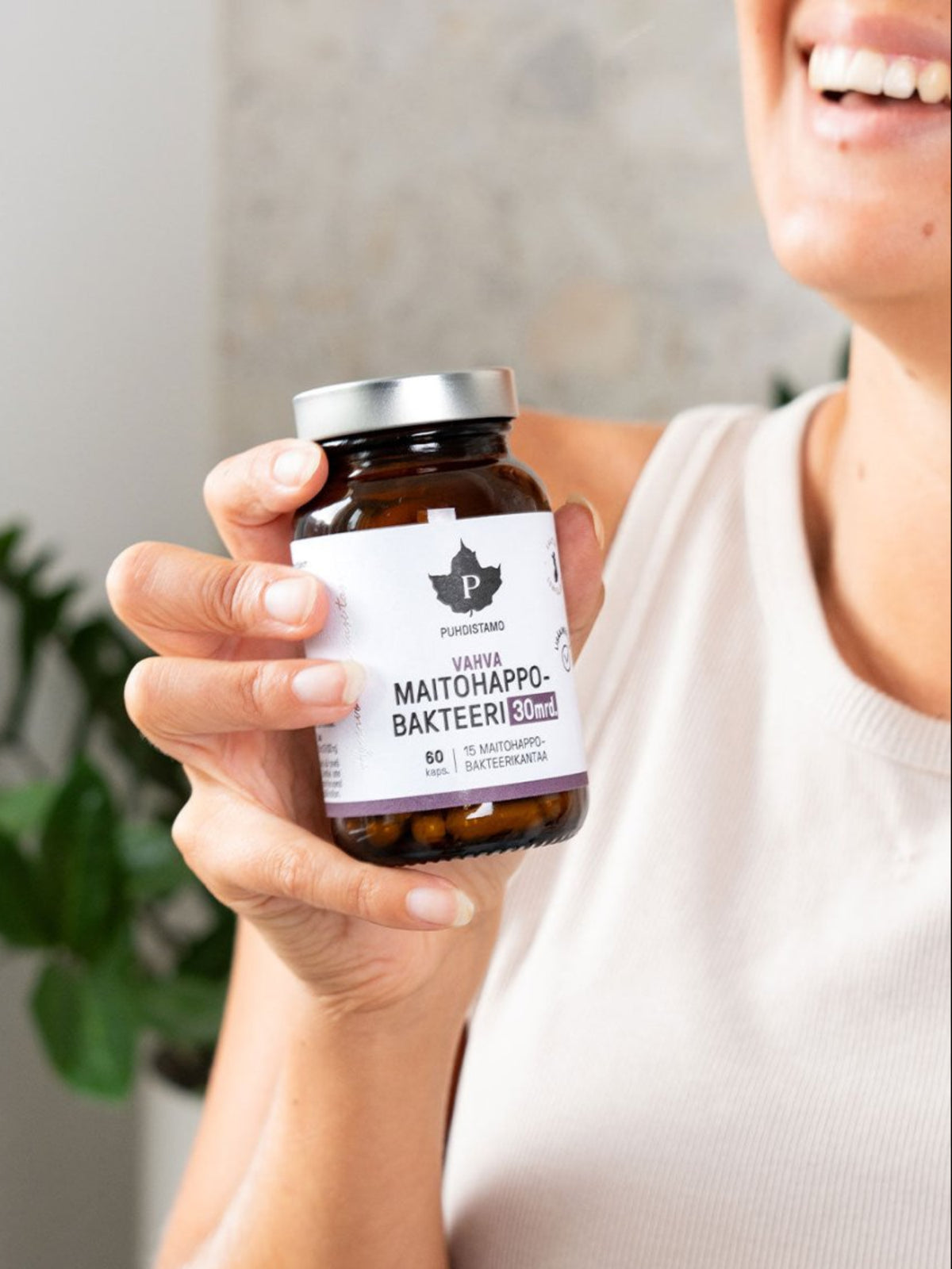 Nainen hymyilee ja pitää kädessään Puhdistamon Vahva aMaitohappobakteeri 30 mrd. 60 kapselin purkkia